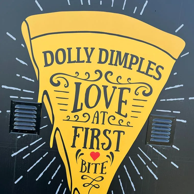 Veggmaleri av et gult pizzastykke med teksten Love at first bite