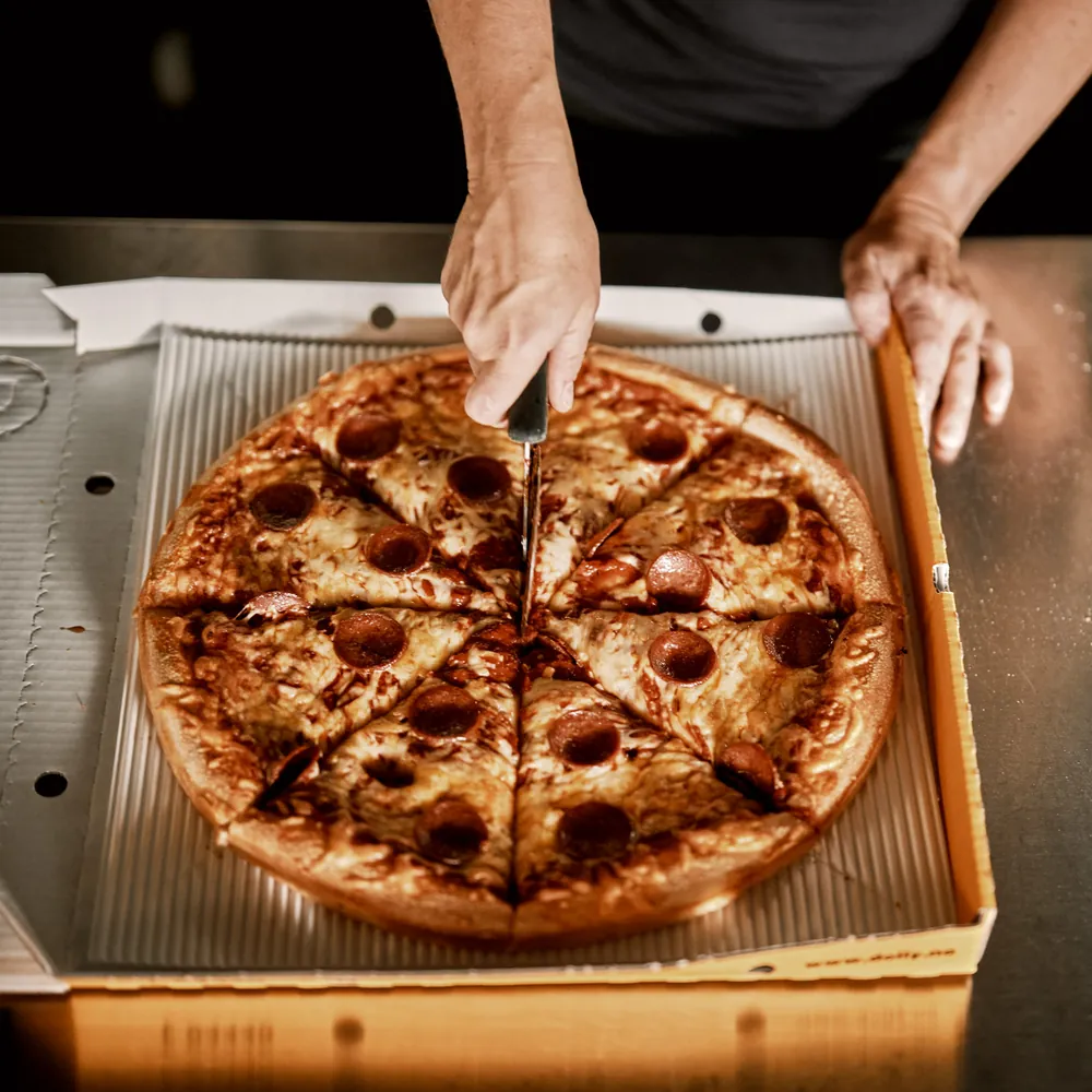 En pepperonipizza blir delt i stykker i en Dolly-eske