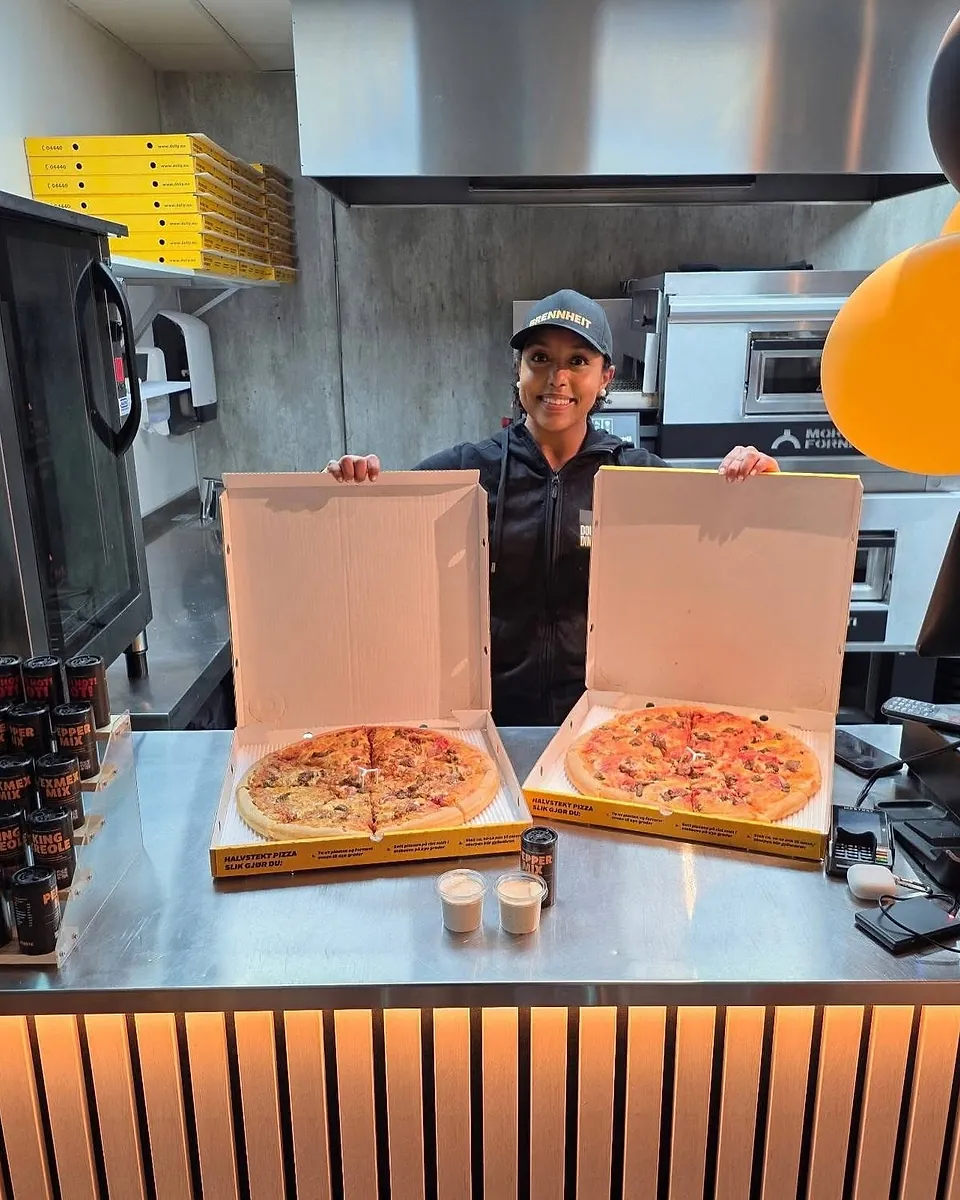 En ansatt hos Dolly Dimples viser fram to pizzaer i åpne esker ved disken